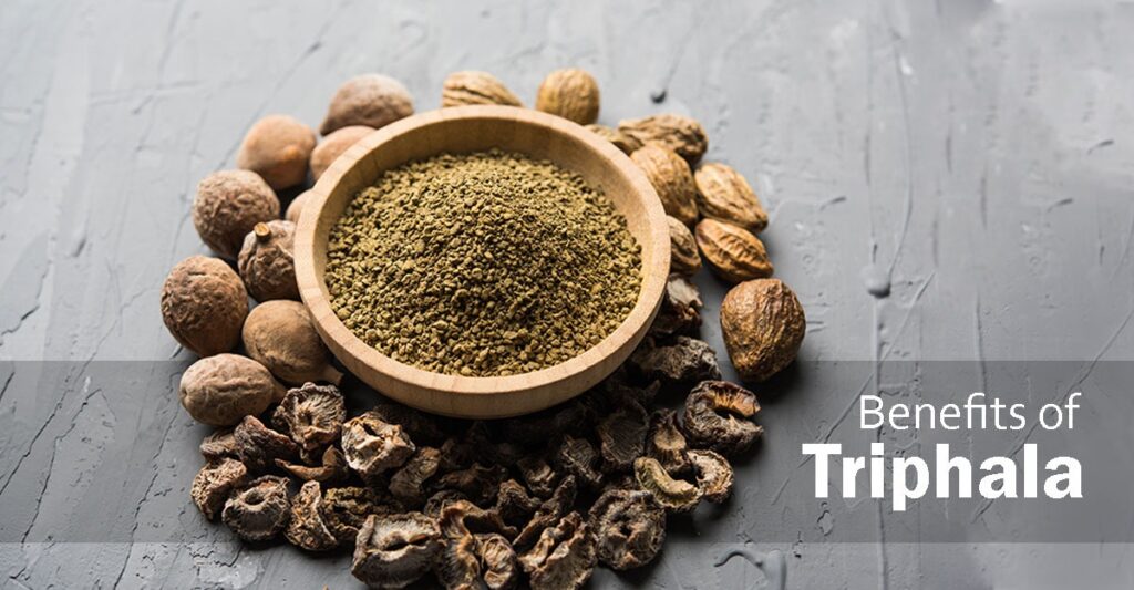 A bowl of Triphala powder with Amalaki, Bibhitaki, and Haritaki fruits, highlighting its benefits for digestion and glowing skin|fitgood360.com
